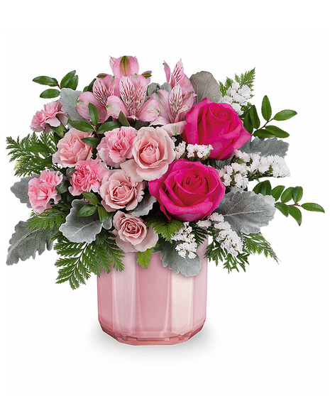 A mix of pink roses and spray roses and carnations arranged in a pink vase.