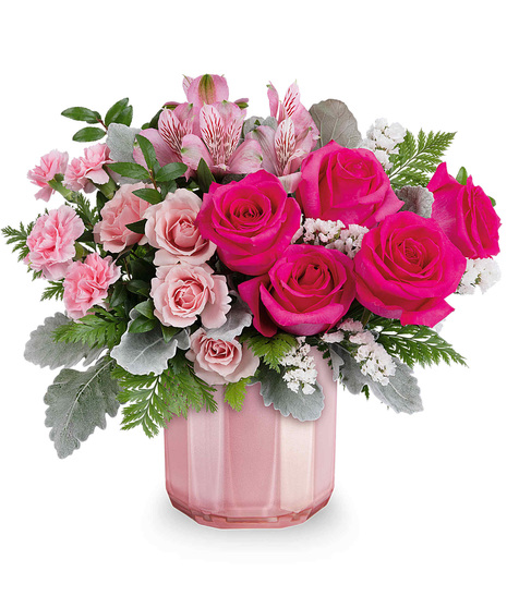 A mix of pink roses and spray roses and carnations arranged in a pink vase.